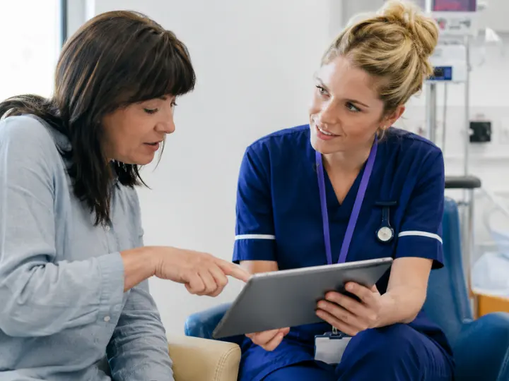 UK nurse and adult patient reviewing a care plan on a tablet, discussing treatment options through shared decision-making in a modern healthcare setting.
