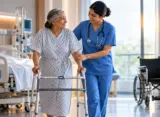 Nurse assisting a patient with early ambulation using a walker in a hospital